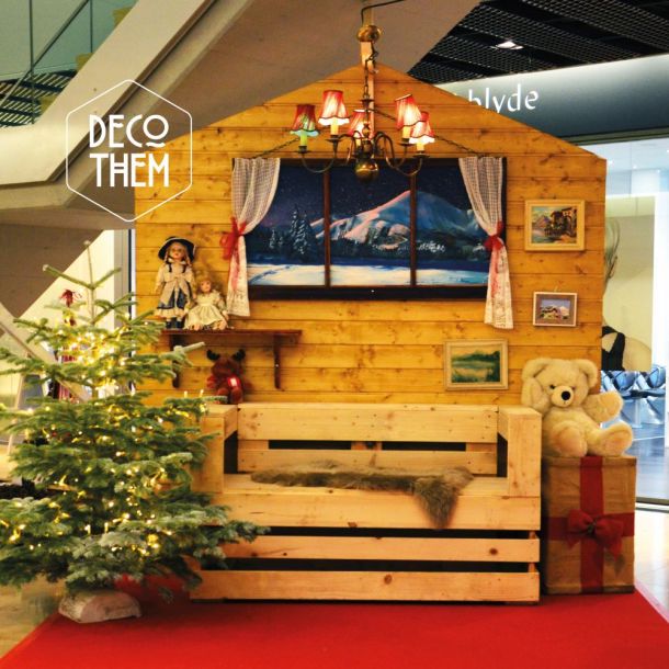 Stand photo St-Nicolas, canapé palette, paroi de chalet, peinture hivernale, sapin illuminé, paquet cadeau, ours en peluche, lustre
